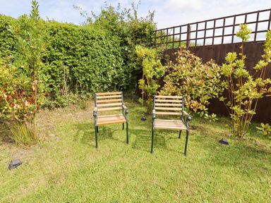 Two wooden chairs on grass next to plants and a wooden fence in a garden at Meols Holiday Lodge in Meols