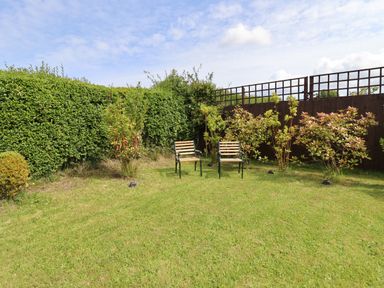 A garden with green grass two chairs and plants along a fence at Meols Holiday Lodge in Meols