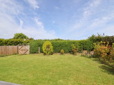 A garden with green grass bushes a wooden fence and two chairs at Meols Holiday Lodge in Meols