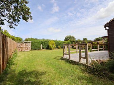 A grassy backyard with wooden fence and gate and a wooden deck attached to a building at Meols Holiday Lodge in Meols
