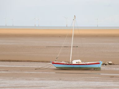 A sailboat stranded on a sandy beach during low tide with wind turbines in the background at Meols Holiday Lodge in Meols