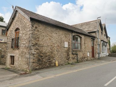An old stone building with windows and doors along a paved road at Coach House in Arnside