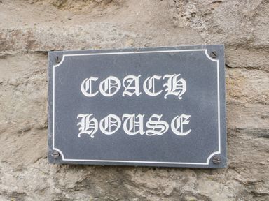 A black rectangular plaque with white decorative font reading Coach House mounted on a stone wall at Coach House in Arnside