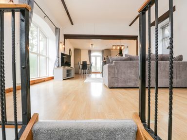An open living and dining area with a grey couch wooden floor and large arched window at Coach House in Arnside