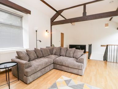 A living room with a large gray sectional sofa wooden floor and exposed ceiling beams at Coach House in Arnside