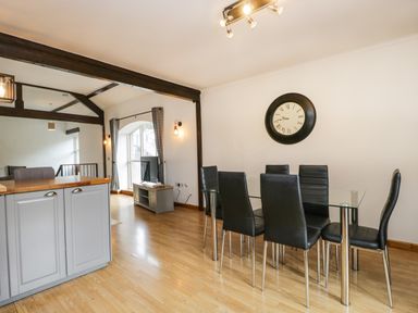 A dining area with a glass table and six black chairs next to a kitchen island and a living area with a TV at Coach House in Arnside