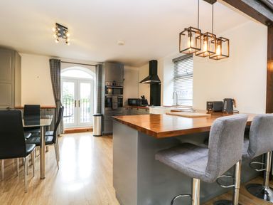 A kitchen and dining area with stools at a wooden island and glass table with black chairs at Coach House in Arnside