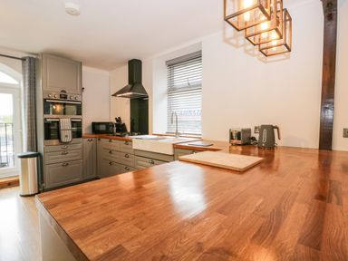 A kitchen with wooden countertops gray cabinets a sink toaster kettle microwave and oven at Coach House in Arnside