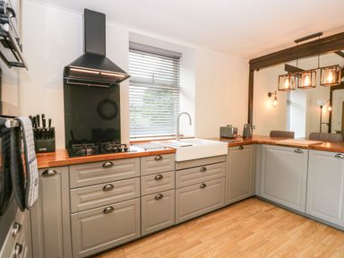 A kitchen with gray cabinets a wooden countertop a gas stove a white sink and modern lighting at Coach House in Arnside