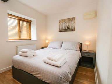 A bedroom with a double bed two bedside tables with lamps a window with blinds and a wall painting at Coach House in Arnside
