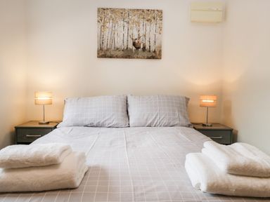 A bedroom with a bed with gray checkered bedding two bedside tables with lamps and a painting of a deer in the forest at Coach House in Arnside