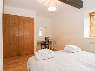 A bedroom with a double bed with towels on top a desk with a mirror and chair by a window with blinds and wooden double doors at Coach House in Arnside