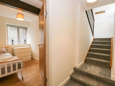 A hallway with carpeted stairs and a room with a bed dresser and window blinds at Coach House in Arnside