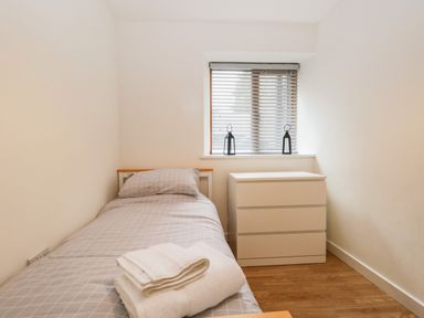 A small bedroom with a single bed a dresser and two lanterns on the windowsill at Coach House in Arnside