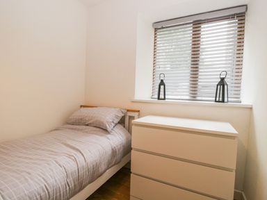 A bedroom with a single bed with checked bedding and a white chest of drawers under a window with blinds and two lanterns at Coach House in Arnside