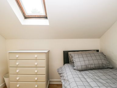 A bedroom with a bed with checkered bedding a white chest of drawers and a skylight window at Coach House in Arnside