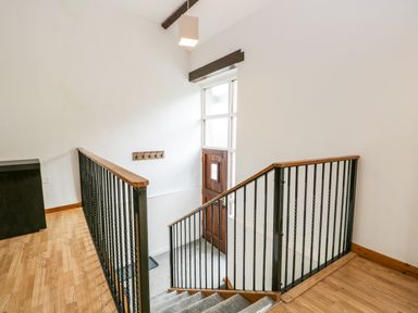 A stairway with black metal railings and wooden handrails leading down to a wooden door with glass panels at Coach House in Arnside
