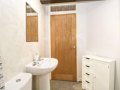 A bathroom with a white pedestal sink with soap dispenser a wooden door a white cabinet with drawers and a toilet at Coach House in Arnside