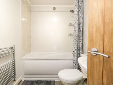 A bathroom with a bathtub shower combination a toilet a sink a towel rack and a wooden door at Coach House in Arnside