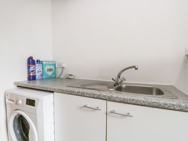 A laundry room with a washing machine sink and cleaning supplies on the counter at Coach House in Arnside