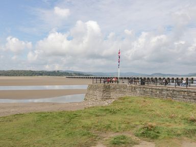 A stone pier with benches and a flagpole near a sandy beach and grassy area at Coach House in Arnside