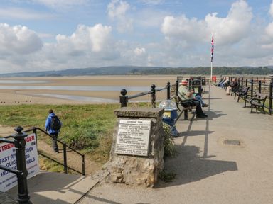 A pier with benches and people sitting near a sandy beach and water at Coach House in Arnside
