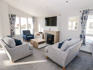 A living room with two grey sofas blue armchair coffee table fireplace and wall mounted television at Dershel Lodge in Southerness