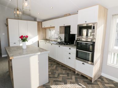 A kitchen with white cabinets a kitchen island with flowers and built in oven and microwave at Dershel Lodge in Southerness