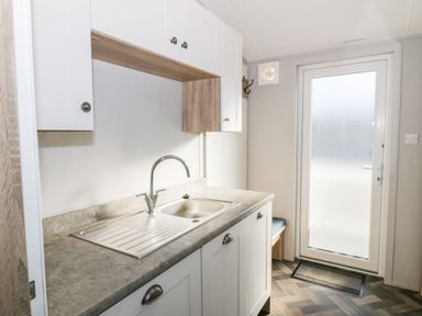 A kitchen sink with white cabinets and a glass door at Dershel Lodge in Southerness