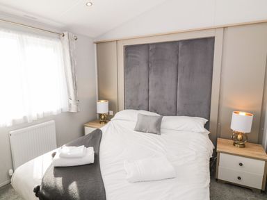 A bedroom with a large bed bedside tables lamps and a window at Dershel Lodge in Southerness