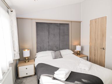 A bedroom with a double bed two bedside tables with lamps a window and a wooden door at Dershel Lodge in Southerness