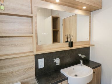 A bathroom sink with a mirror and wooden shelves at Dershel Lodge in Southerness