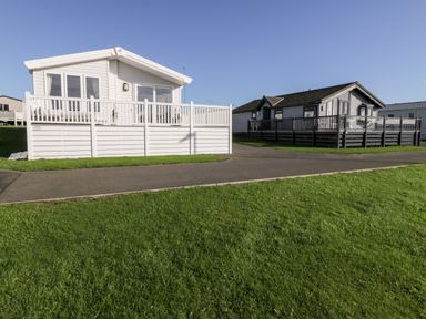 Two mobile homes with fenced decks on a paved path and grass at Dershel Lodge in Southerness
