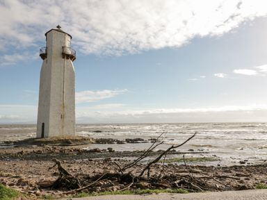 A lighthouse standing on a rocky shoreline with waves in the sea and a partly cloudy sky at Dershel Lodge in Southerness