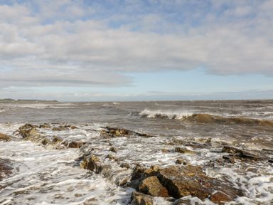 A rocky shoreline with waves crashing and a cloudy sky at Dershel Lodge in Southerness