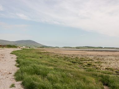 A coastal landscape with grassy shore, sandy beach, and distant hills at Dershel Lodge in Southerness