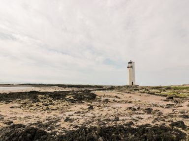 A rocky shoreline with a tall white lighthouse under a cloudy sky at Dershel Lodge in Southerness