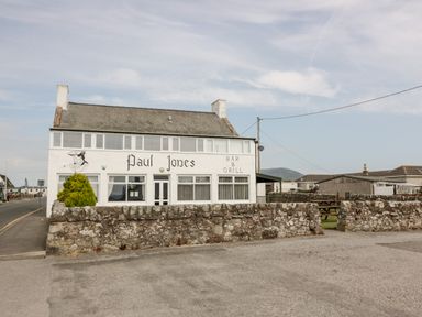 A bar and grill building named Paul Jones with a stone wall and picnic tables outside