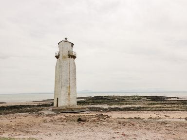 A lighthouse on a rocky and sandy shore with the sea and distant mountains in the background at Dershel Lodge in Southerness
