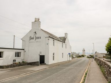 A street view with a white building called Paul Jones Bar and Grill and a distant lighthouse at Dershel Lodge in Southerness