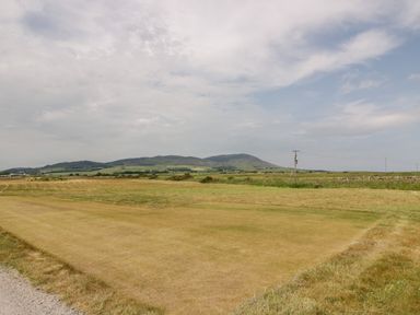 A grassy field with a section of mowed grass and hills in the background at Dershel Lodge in Southerness