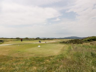 A golf course with players and golf bags on a pathway with hills in the background at Dershel Lodge in Southerness