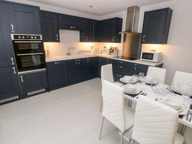 A kitchen with dark cabinets white countertops dining table with white chairs and tableware at LunaRoxx 6 Meadow Gardens Kilgetty