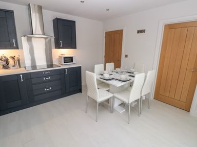 A kitchen with dark cabinets a dining table set for six and two wooden doors at LunaRoxx 6 Meadow Gardens Kilgetty
