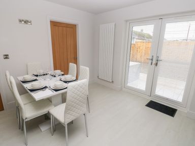 A dining area with a table set for six next to a wooden door and glass double doors with blinds at LunaRoxx 6 Meadow Gardens Kilgetty