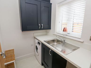 A utility room with a washing machine and sink under a window with blinds at LunaRoxx 6 Meadow Gardens Kilgetty