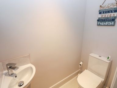 A small bathroom with a white sink and a toilet with a toilet roll holder and a wall decoration at LunaRoxx 6 Meadow Gardens Kilgetty