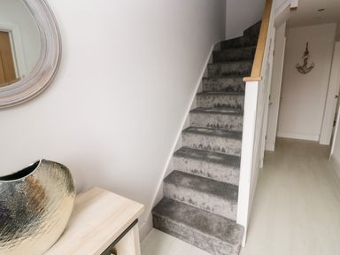 A hallway with carpeted stairs a wooden table a silver vase a round mirror and an anchor decoration on the wall at LunaRoxx 6 Meadow Gardens Kilgetty