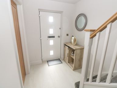 A hallway with a white front door and a small wooden cabinet with a decorative vase and round wall mirror at LunaRoxx 6 Meadow Gardens Kilgetty