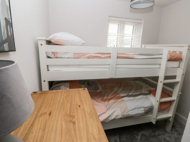 A small bedroom with a white bunk bed a wooden desk and a lamp at LunaRoxx 6 Meadow Gardens Kilgetty